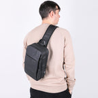 Person wearing a black sling bag on a plain background